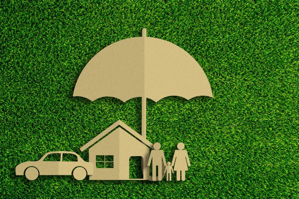 A paper cut out of a car, a house, two people, and an umbrella above them all, lying on astroturf.